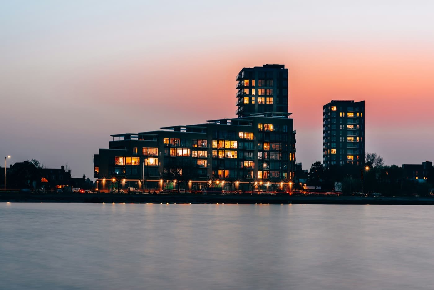 A dark building on the water at blue hour with the skyline behind it